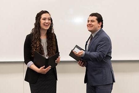 Two college students giving a speech holding notepads