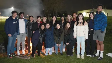 一群16个学生在外面的营火前微笑