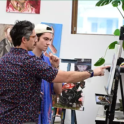 Student and professor at an easel reviewing the student's painting.