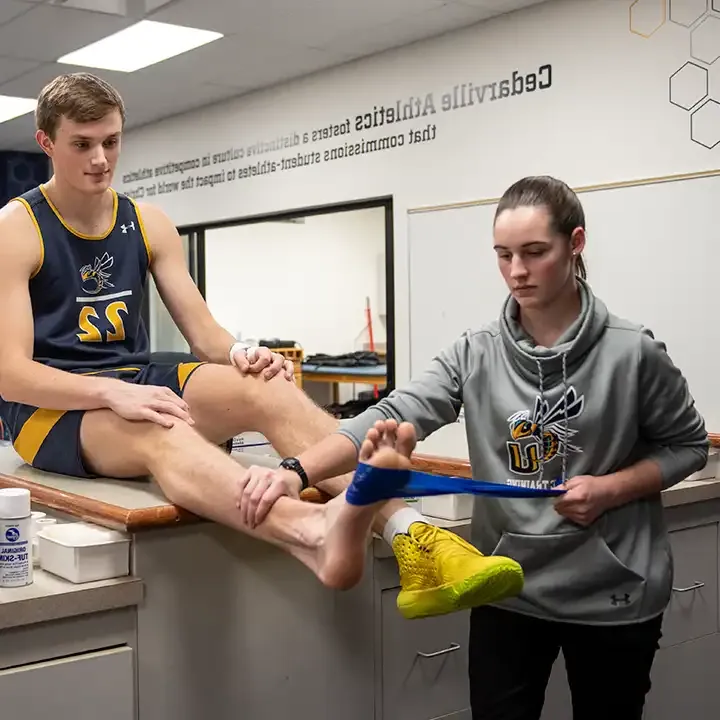 在训练室内，女运动教练正在包扎运动员的脚踝.