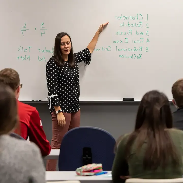 一名女子站在白板前，面前是坐着的学生.